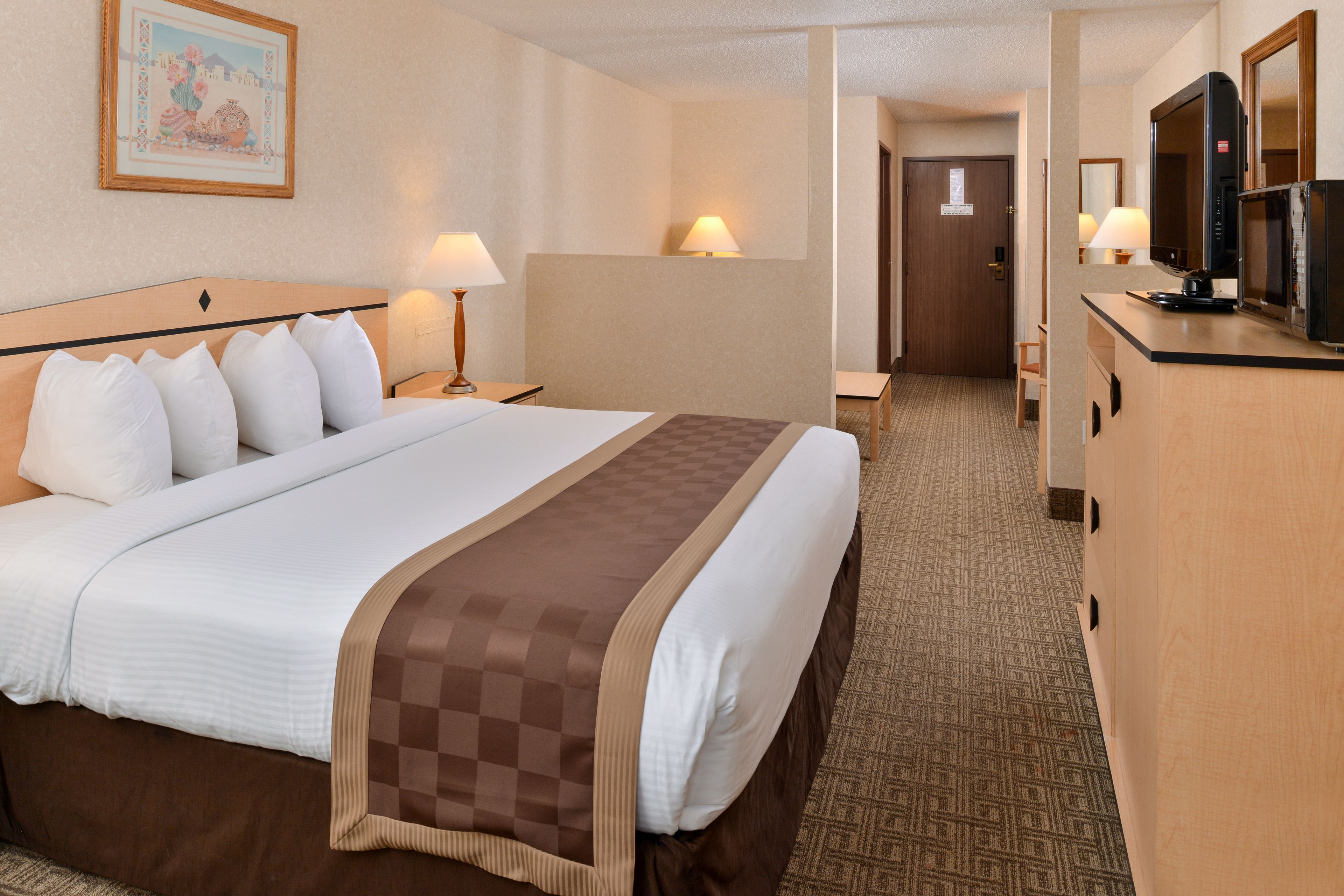 A hotel room with a large bed, two bedside lamps, a television, and a desk with a chair.