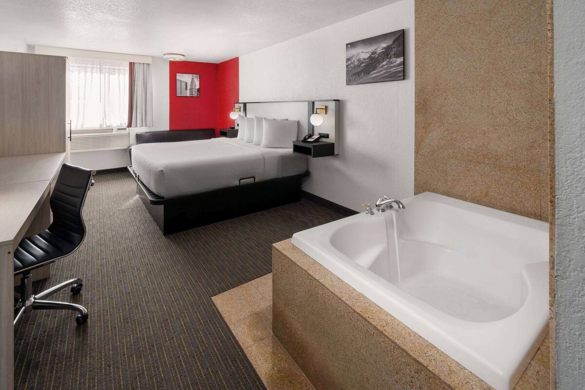 Ein Hotelzimmer mit einem großen Bett, einem Schreibtisch, einem Stuhl, einer Schreibtischlampe, einem Telefon, einem Bild an der Wand und einer Badewanne.