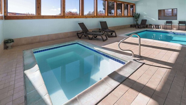 An indoor swimming pool with clear blue water, surrounded by lounge chairs and a tiled floor. - SYLO Hotel Denver Airport, a Ramada by Wyndham (Aurora)