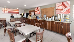 A modern kitchen with wooden cabinets, a dining table with chairs, and various kitchen appliances. - SYLO Hotel Denver Airport, a Ramada by Wyndham (Aurora)