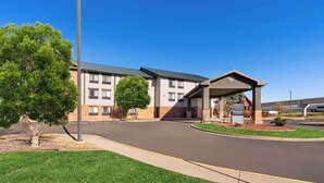 A modern hotel entrance with a covered waiting area, a parking lot, and a clear blue sky. - SYLO Hotel Denver Airport, a Ramada by Wyndham (Aurora)