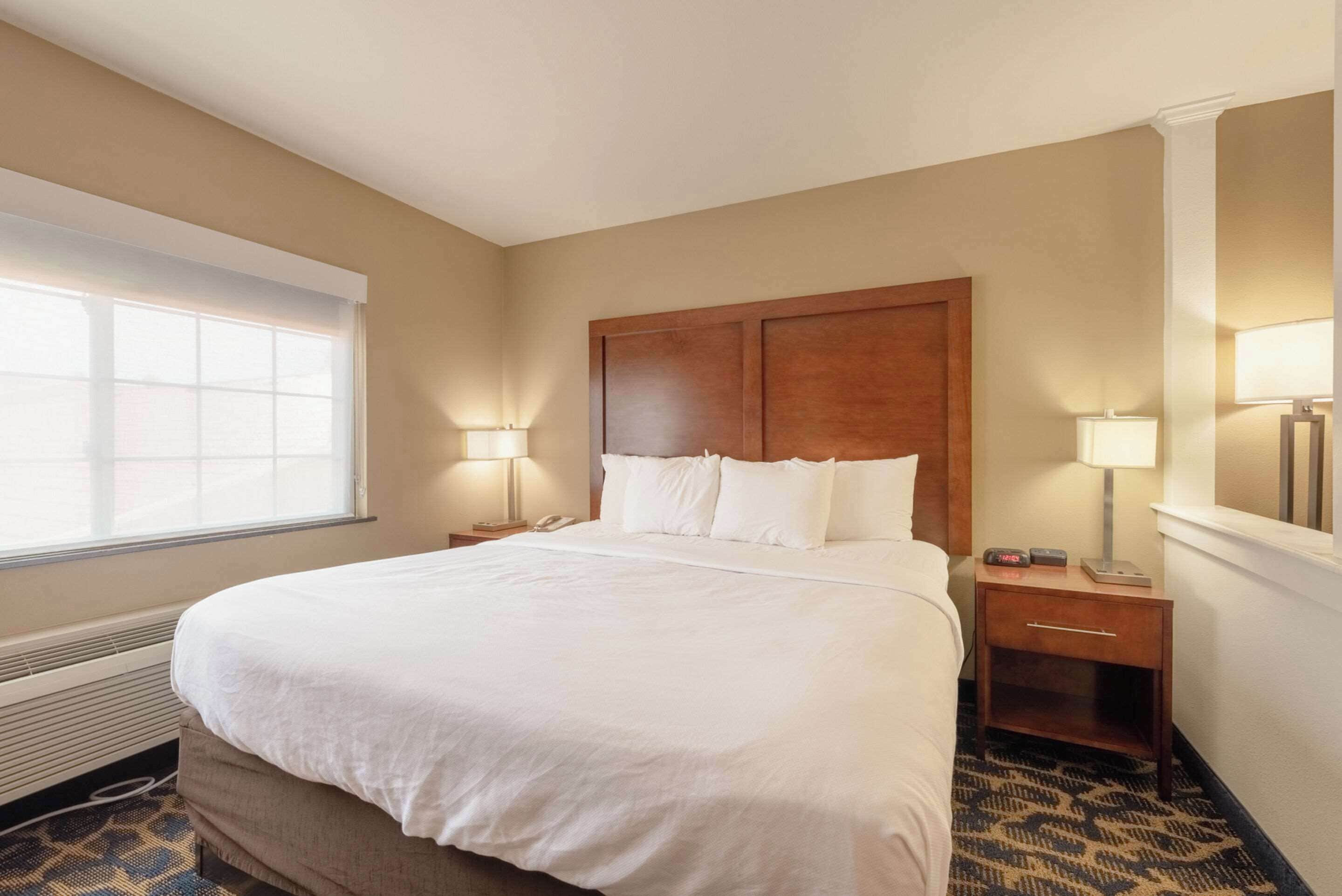 A hotel room with a large bed, two bedside tables with lamps, a heater, and a window with blinds.