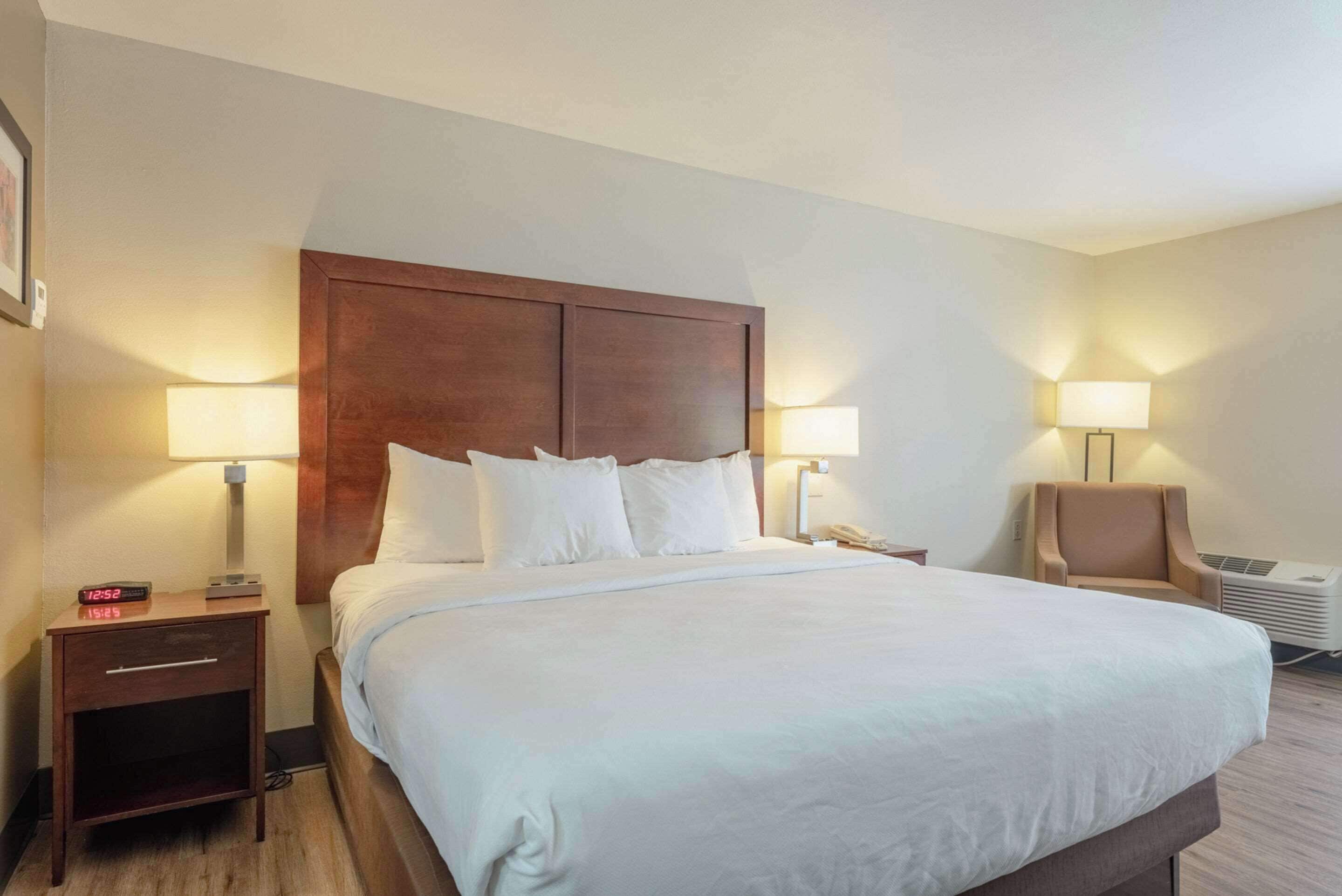 A hotel room with a large bed, two bedside tables, a nightstand, a chair, and a wall-mounted heater.