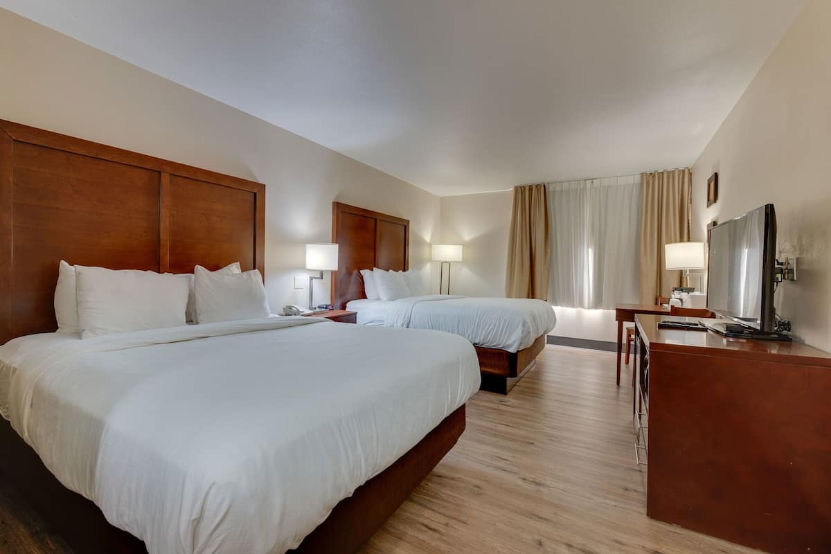 A hotel room with two beds, a desk, a TV, and a lamp.