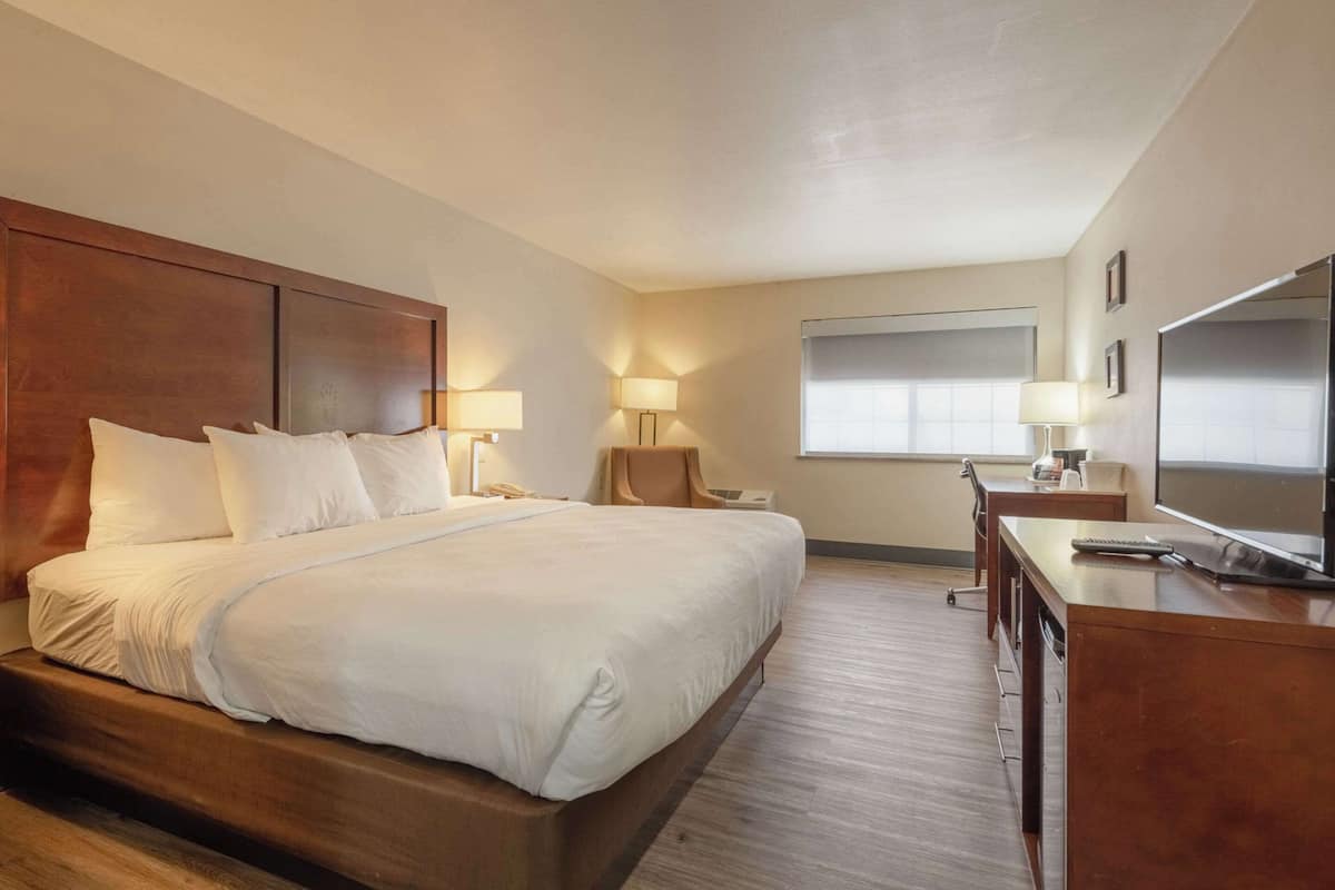 A hotel room with a large bed, bedside lamps, a desk with a chair, and a large window.