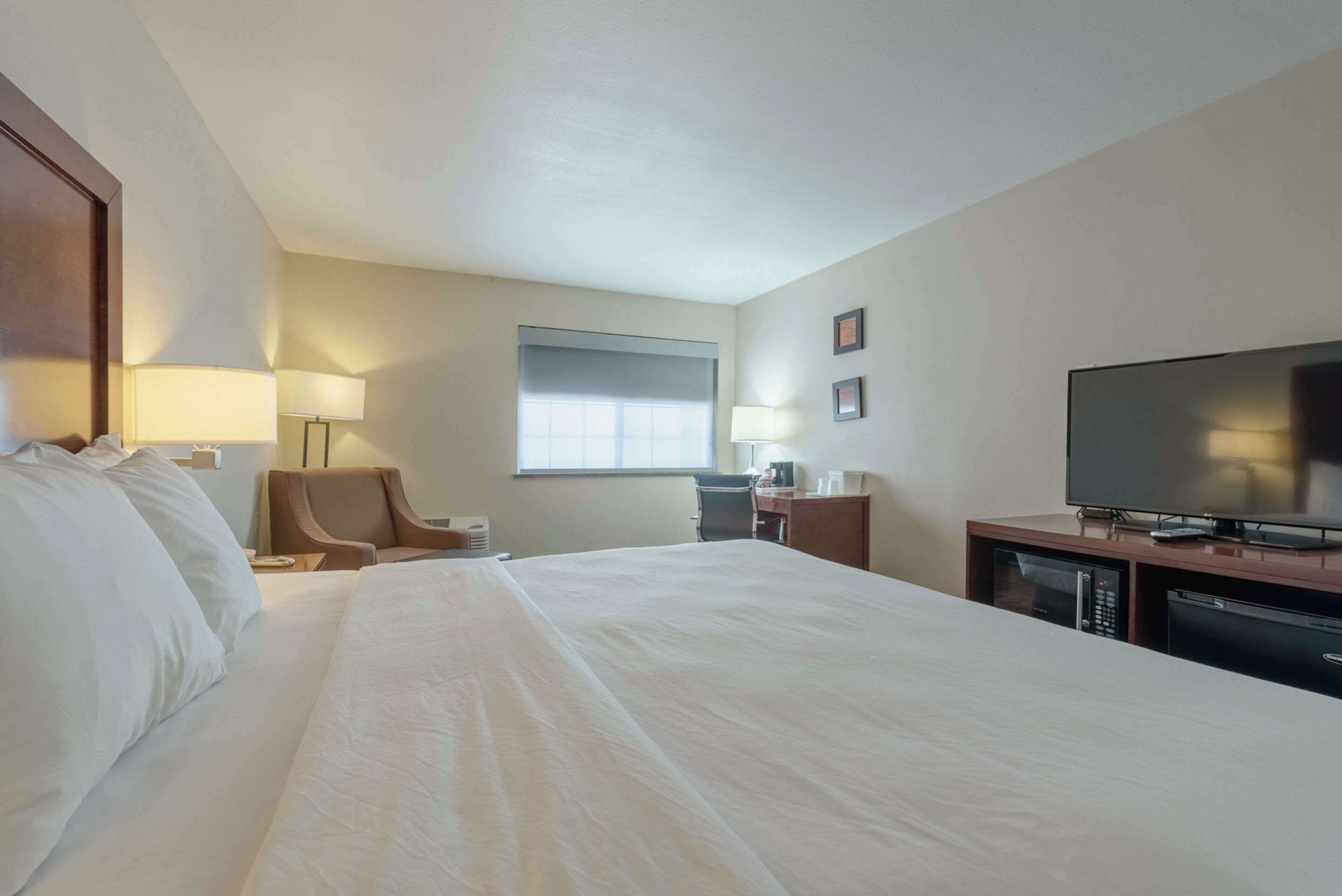 Une chambre d’hôtel avec un grand lit, un bureau doté d’un téléviseur à écran plat, une chaise, une lampe et une fenêtre.