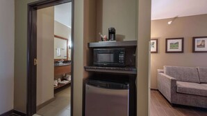 A compact kitchenette with a microwave, coffee maker, and a small refrigerator. A grey sofa is visible in the adjacent living area.