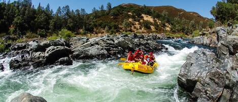 A group of people in a yellow raft navigating a river surrounded by rocky terrain and trees.