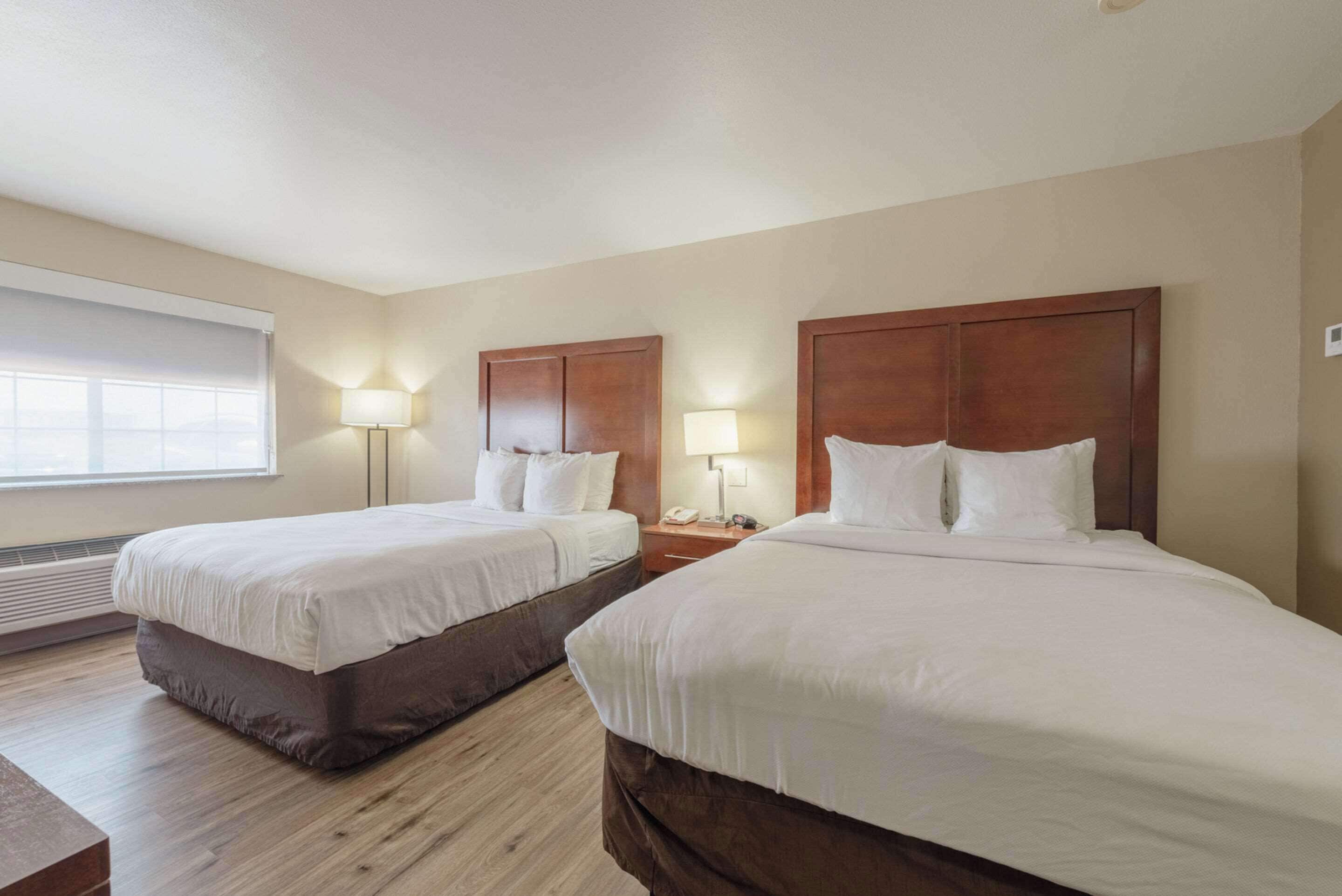 Habitación de hotel con dos camas, una mesita de noche con lámpara, un calentador y una ventana con persianas.