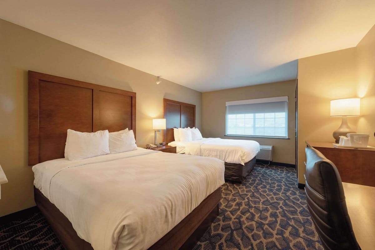 A hotel room with two beds, a desk, and a window.