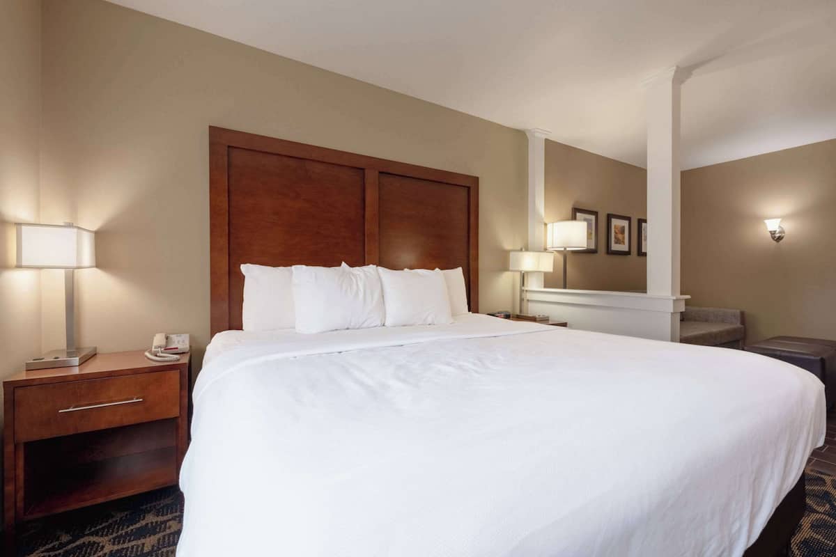 A hotel room with a large bed, a wooden headboard, a nightstand with a lamp, and a small table with a lamp.