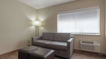 A living room with a grey sofa, a small table, a floor lamp, and a large window with blinds.