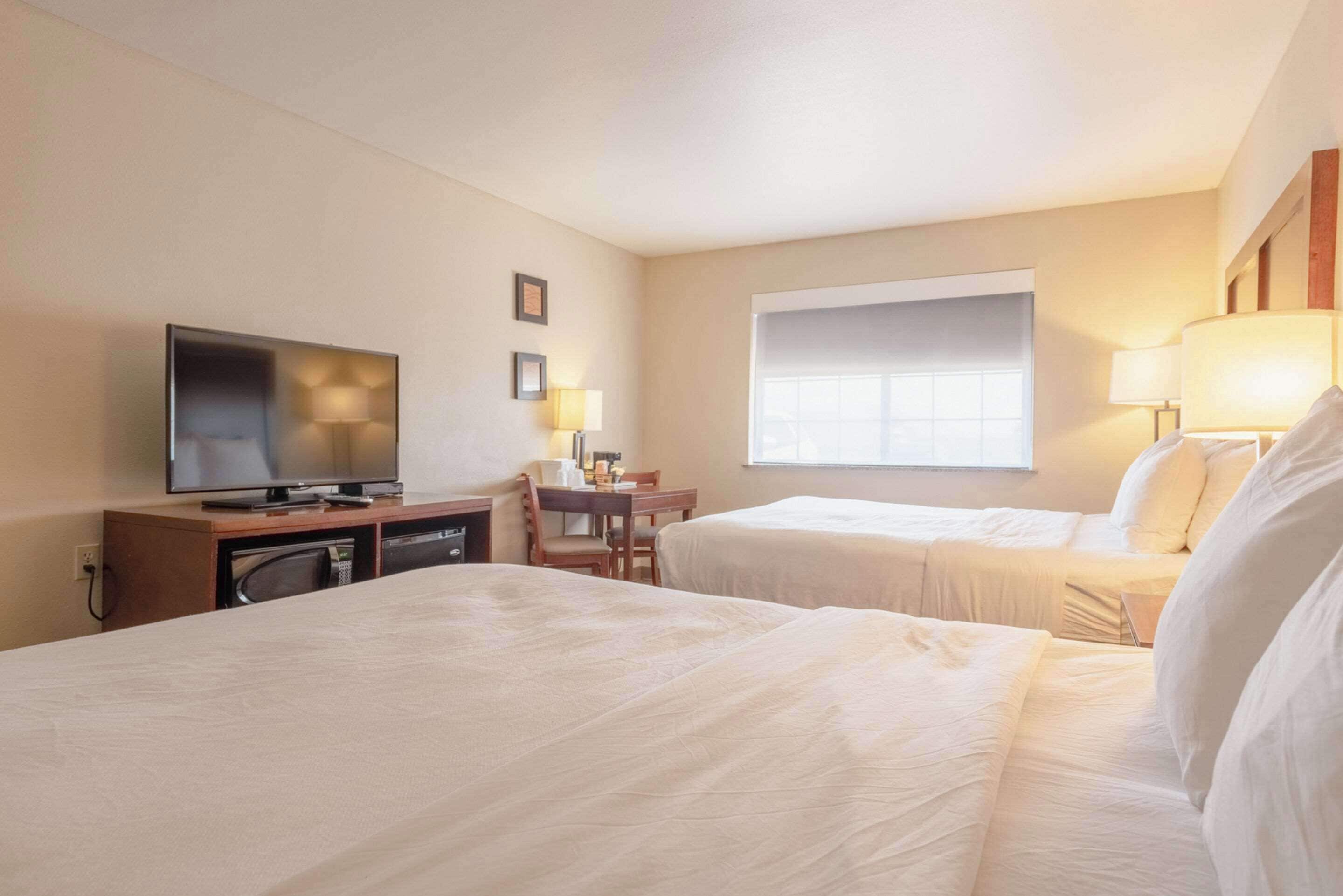 Een hotelkamer met twee bedden, een bureau met stoel, een televisie en een raam met jaloezieën.