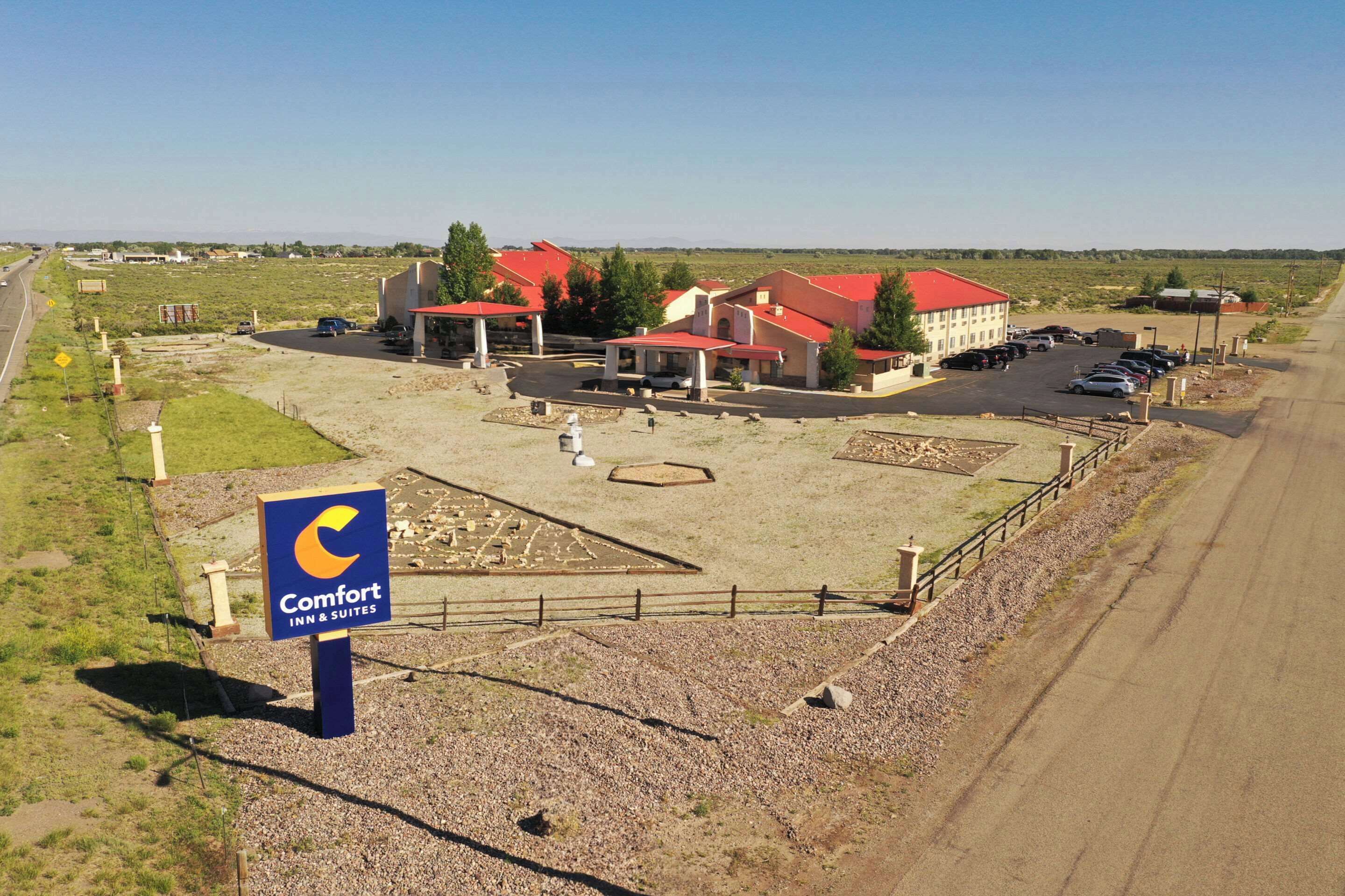 A Comfort Inn & Suites with a red-roofed building, a parking lot, and a gravel area with a sign.