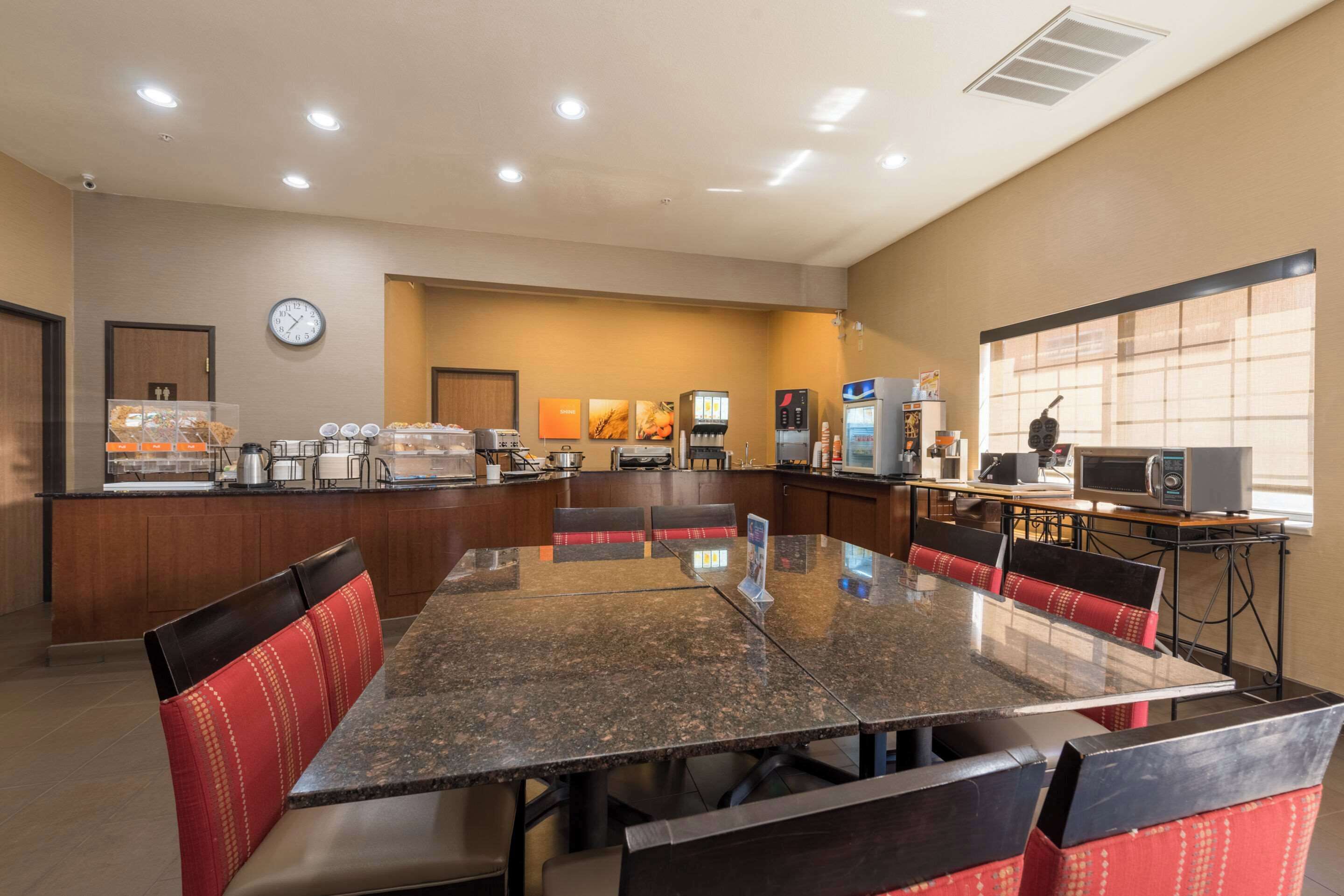 A hotel dining area with a large table, red upholstered booths, a coffee station, and a microwave on a cart.