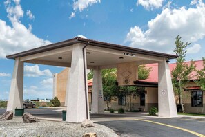 A covered parking area with a canopy, concrete pillars, and a building with a red roof in the background.