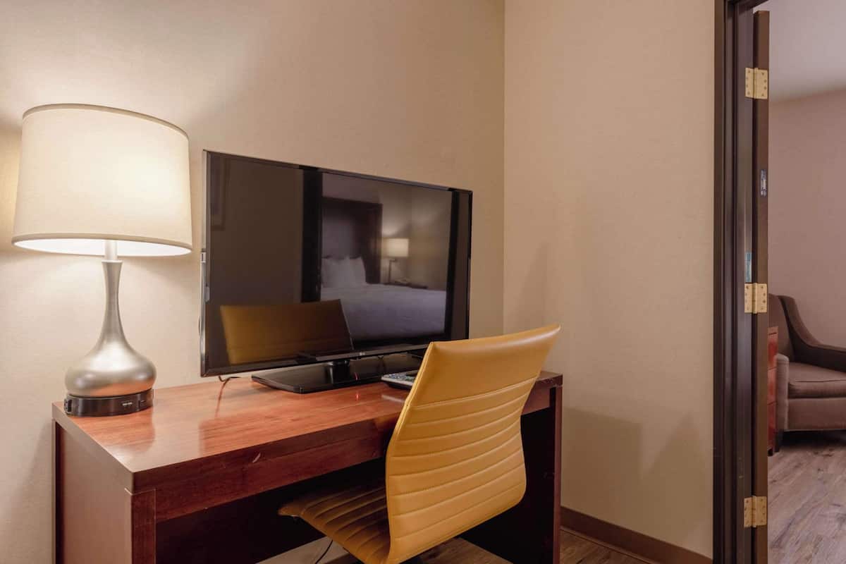 A hotel room with a wooden desk, a modern lamp, a flat-screen TV, and a leather chair.