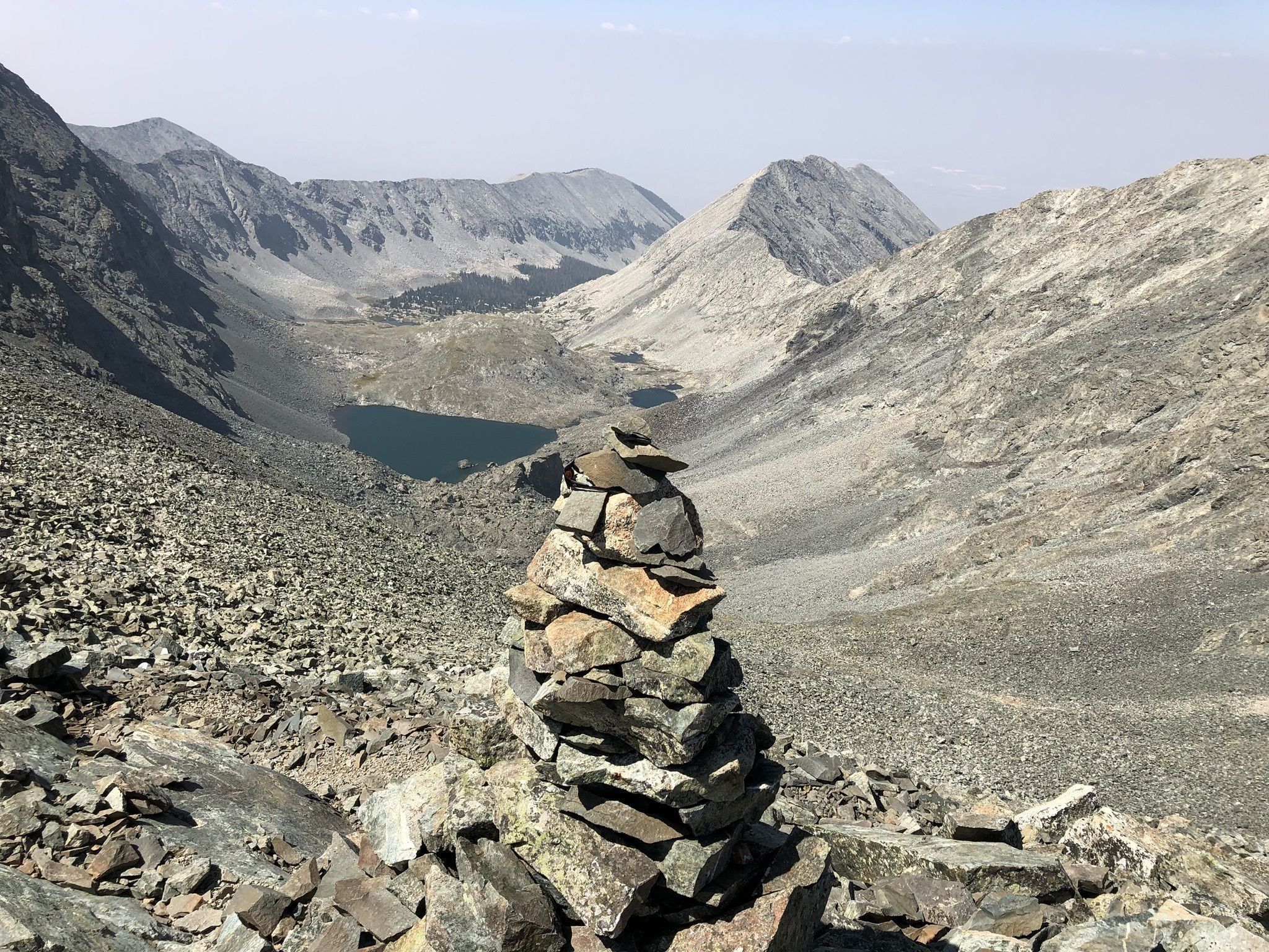 A rocky mountain landscape with a cairn in the foreground and a lake in the valley.