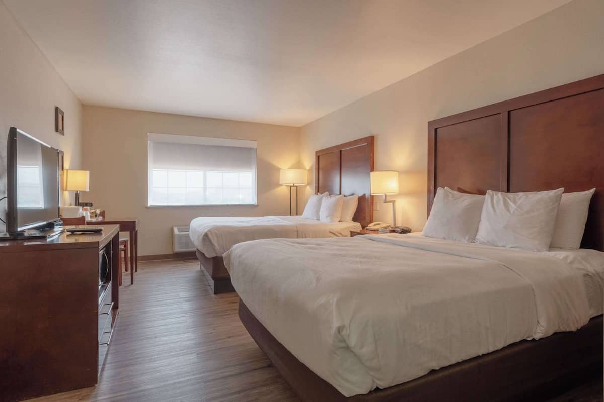 A hotel room with two beds, a desk with a TV, and a window with blinds.