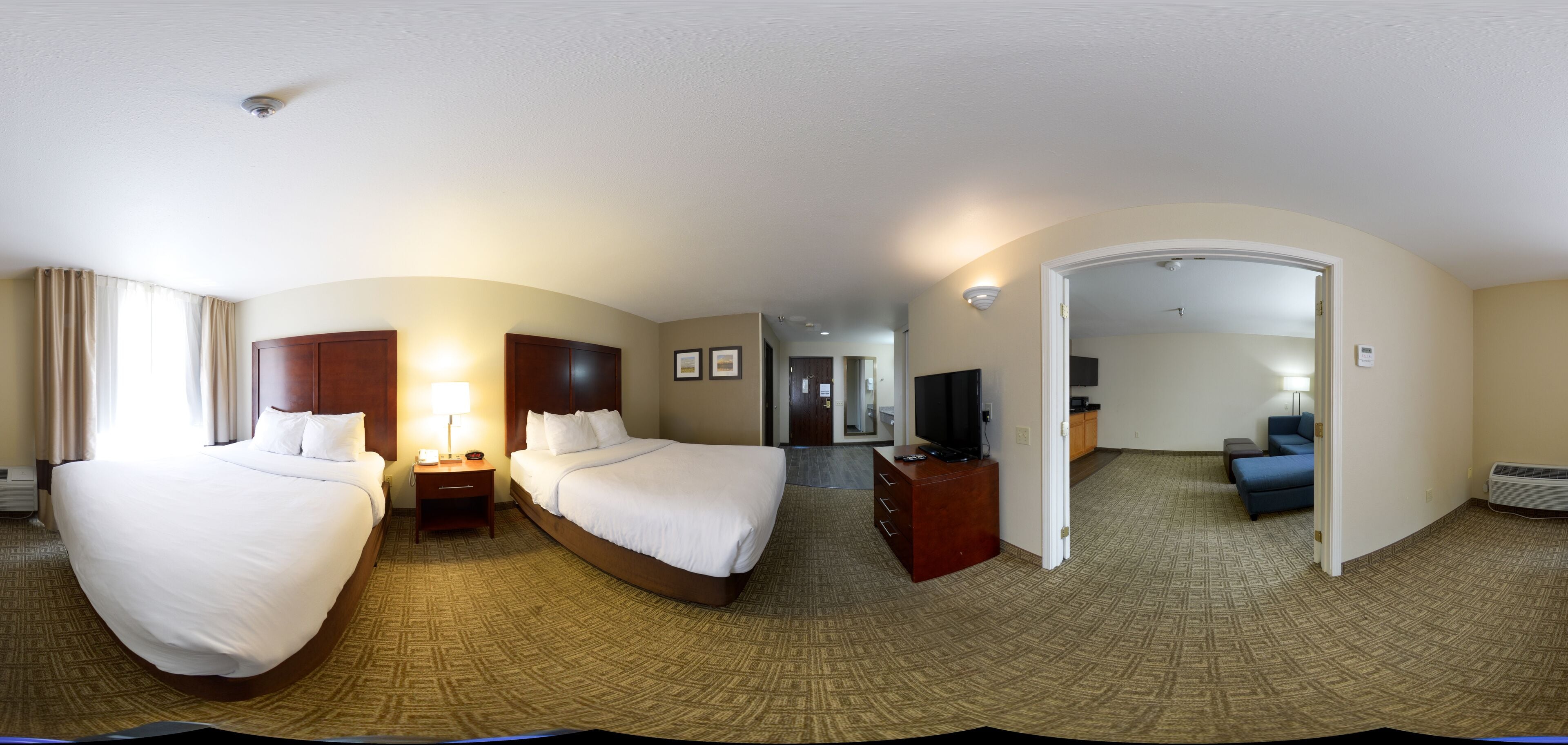 A hotel room with two beds, a desk, a TV, and a bathroom visible through an open door.