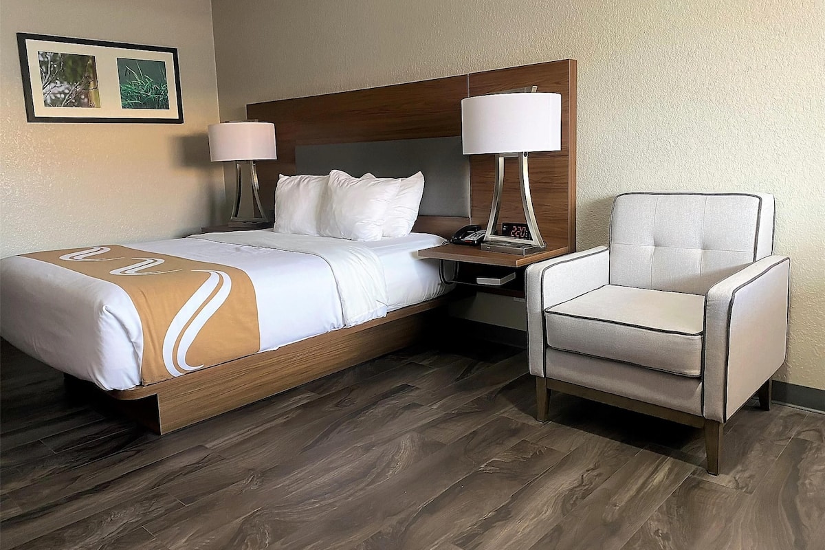 Ein Hotelzimmer mit einem Bett, zwei Nachttischlampen, einem Sessel und einem gerahmten Bild an der Wand.