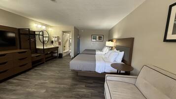 A hotel room with a bed, a sofa, a TV, a bathroom, and a mirror.