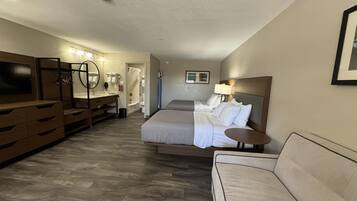 Una habitación de hotel con cama, sofá, televisión, baño y escritorio.
