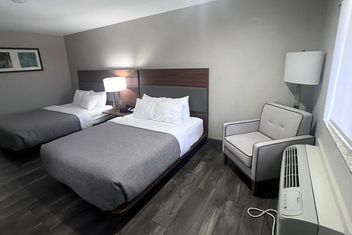 Ein Hotelzimmer mit zwei Betten, einem Sessel, einem Schreibtisch mit Lampe und einem Heizgerät.