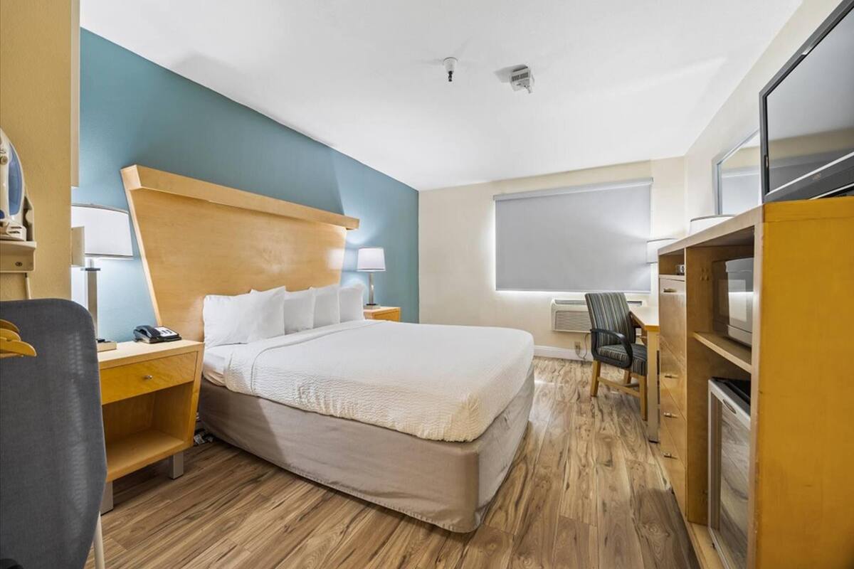 A hotel room with a large bed, a desk, a chair, and a television.