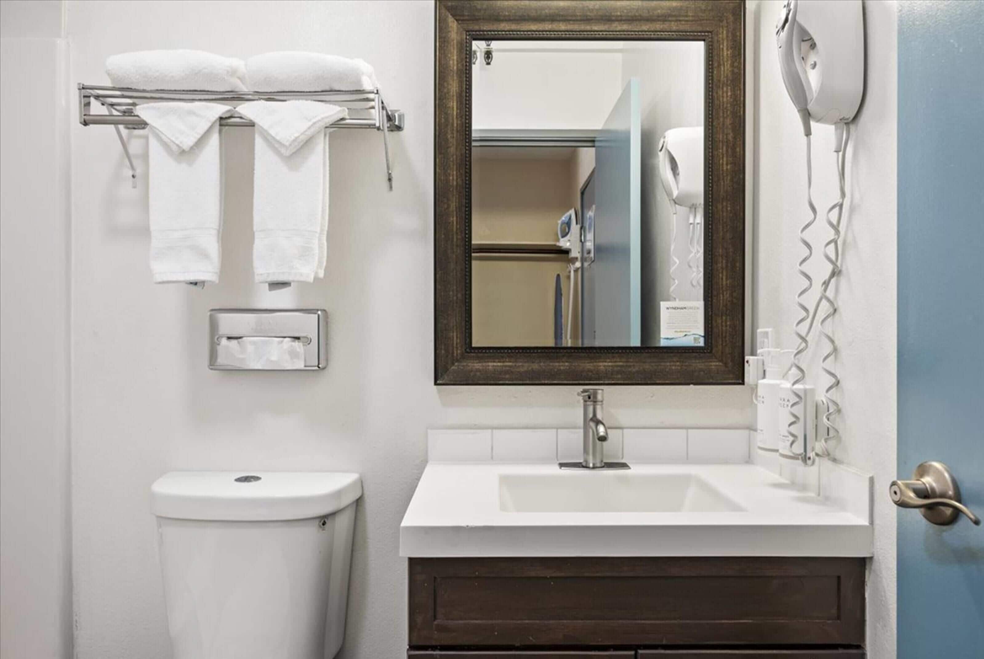 A bathroom with a white sink, a mirror, a towel rack with towels, a toilet, and a hairdryer mounted on the wall.