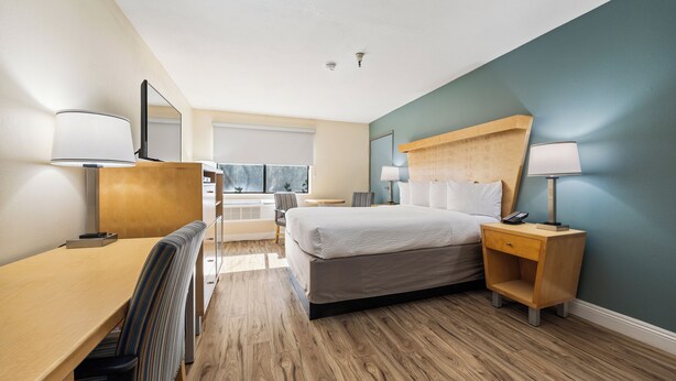 A modern hotel room with a wooden desk, a bed with a headboard, a nightstand, and a chair. - Days Inn by Wyndham Woodland (Woodland)
