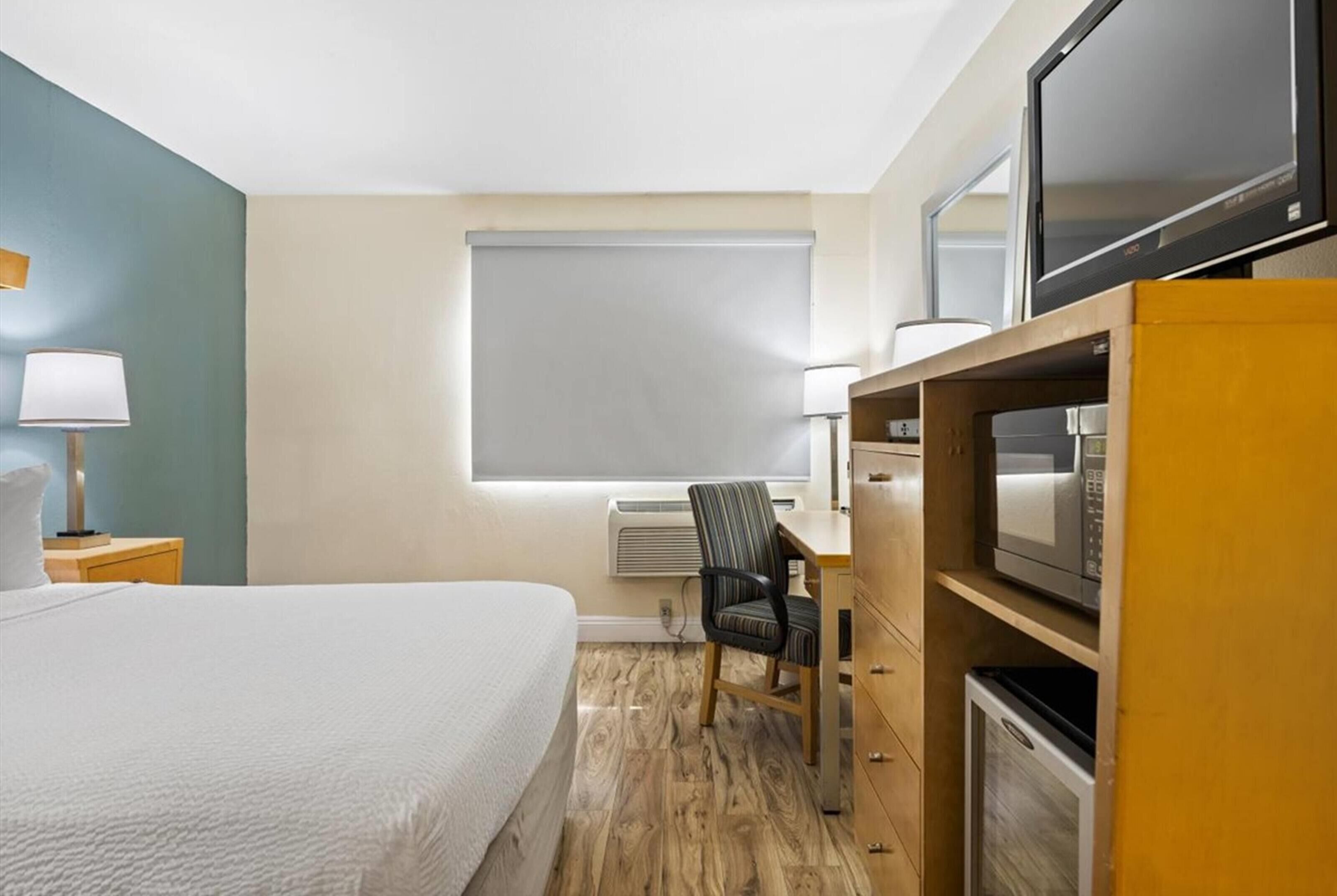 A hotel room with a bed, desk, chair, television, and microwave.