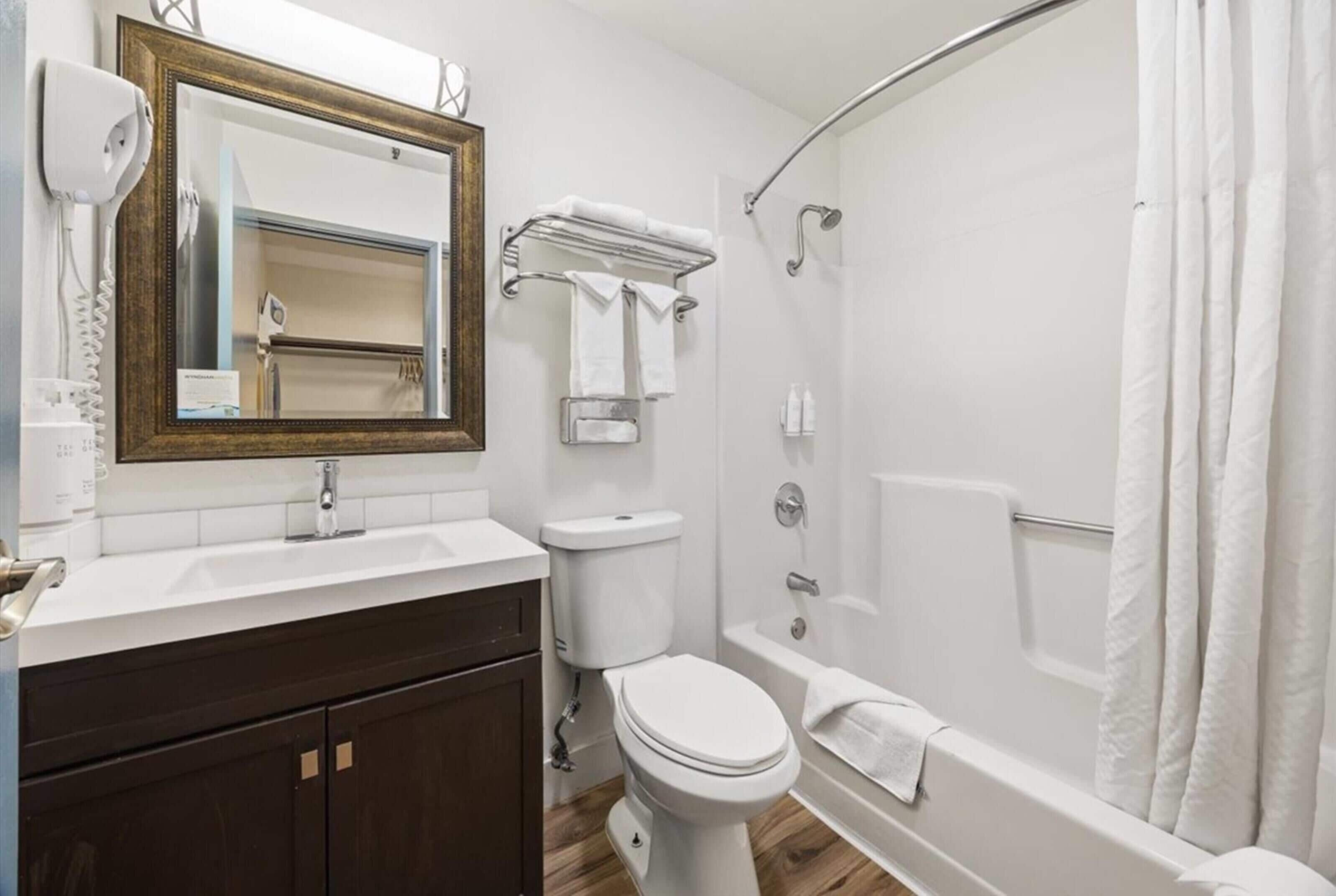 A modern bathroom with a white sink, dark wooden cabinets, a toilet, a bathtub, and a shower.