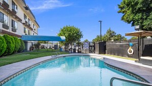 A swimming pool with a clear blue water, surrounded by a fence, and a building with a blue awning in the background. - Days Inn by Wyndham Woodland (Woodland)