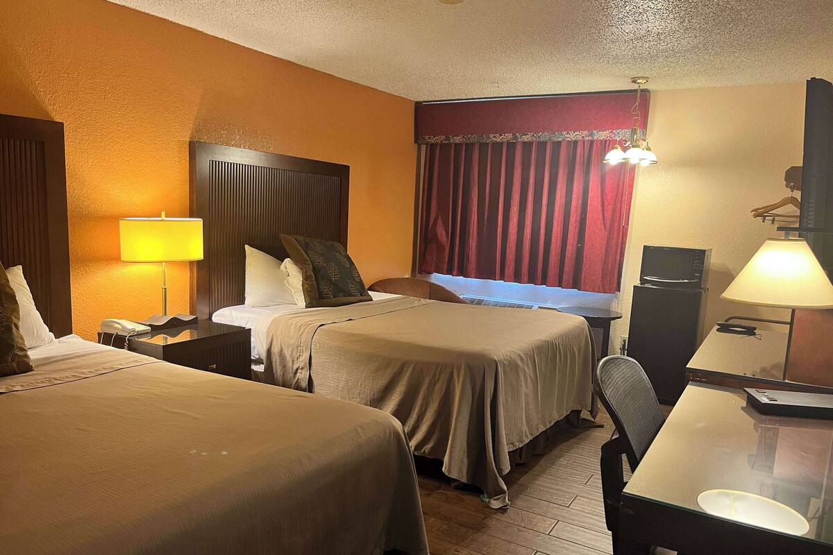A hotel room with two beds, a desk, a chair, a telephone, a microwave, and a television.