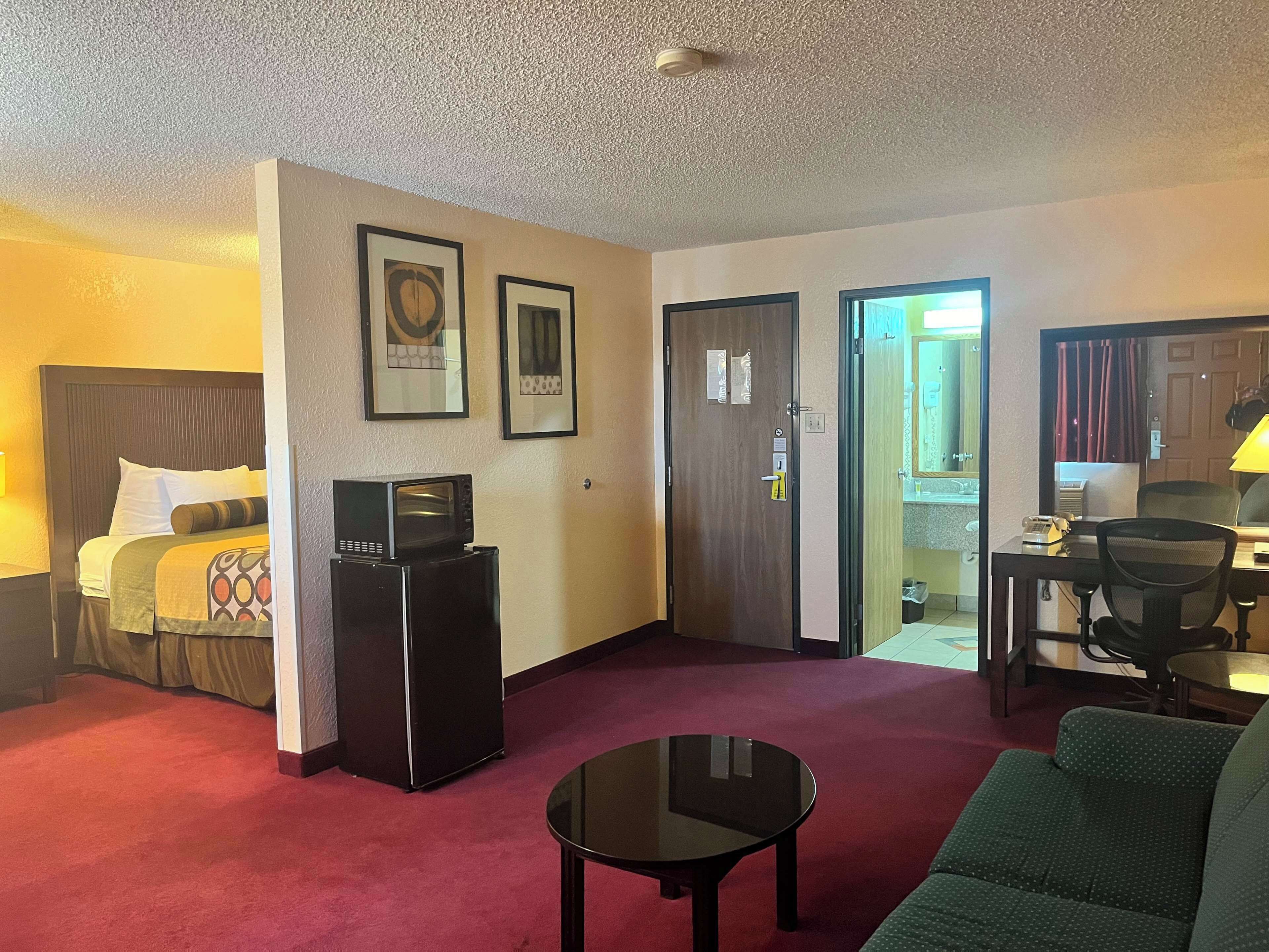 A hotel room with a bed, a desk, a chair, a microwave, and a refrigerator.