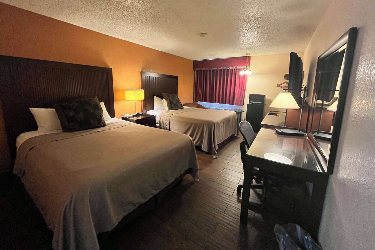 A hotel room with two beds, a desk, a chair, a TV, and a lamp.