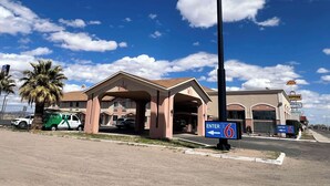 A motel with a prominent '6' sign, a covered parking area, and a clear sky. - Motel 6 Deming, NM (Deming)