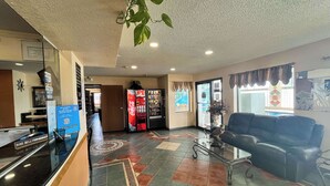 A reception area with a glass counter, a Coca-Cola refrigerator, a seating area with a couch, and a decorative plant. - Motel 6 Deming, NM (Deming)