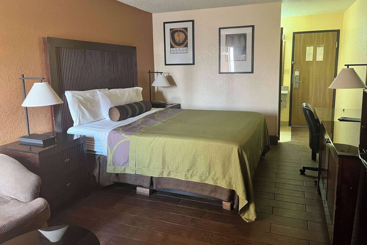 A hotel room with a bed, bedside tables, a chair, a desk, and a door.