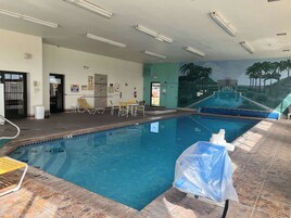 Una piscina interior con agua cristalina, suelo de baldosas y un mural de paisaje tropical.