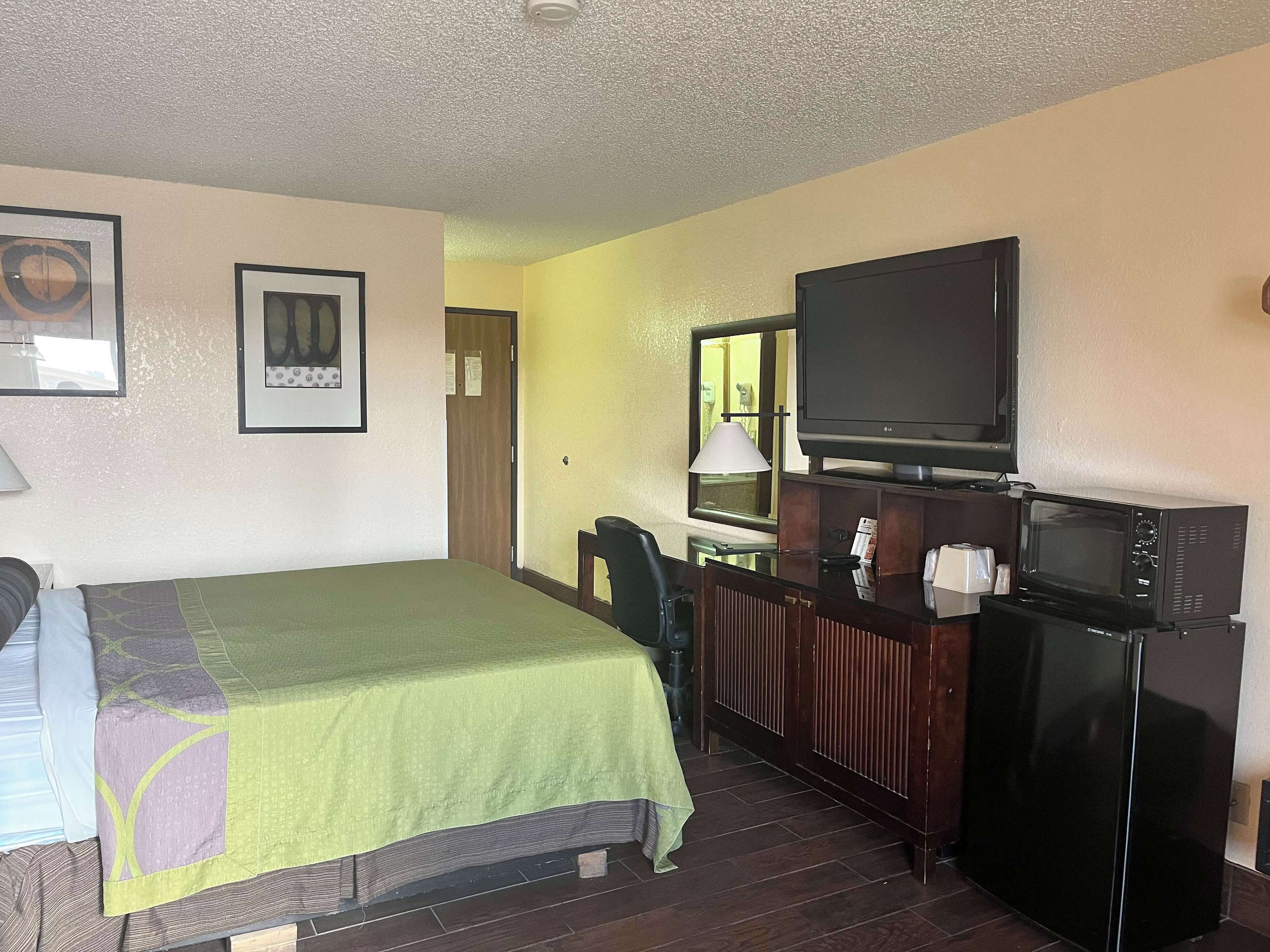 Habitación de hotel con cama, escritorio, televisor, microondas y una silla.