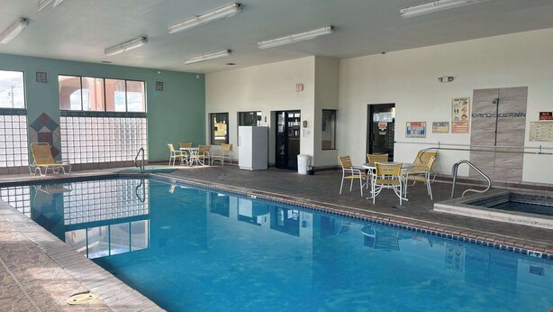 An indoor swimming pool with clear water, surrounded by tiled walls and a tiled floor. There are several lounge chairs and tables around the pool area. - Motel 6 Deming, NM (Deming)