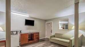 A hotel room with a kitchenette, a flat-screen TV mounted on the wall, a sofa, and a mirror.