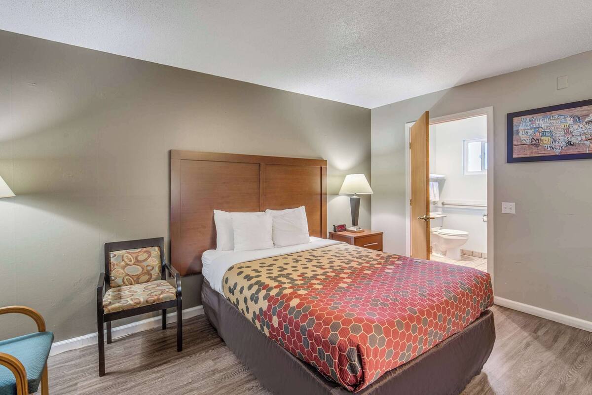 Camera d'albergo con un letto, una poltrona, un comodino e un bagno visibile attraverso una porta aperta.