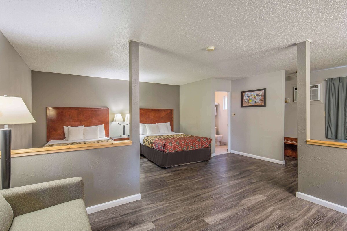 Habitación de hotel con dos camas, cabecera de madera, mesita de noche con lámpara y un espejo grande.