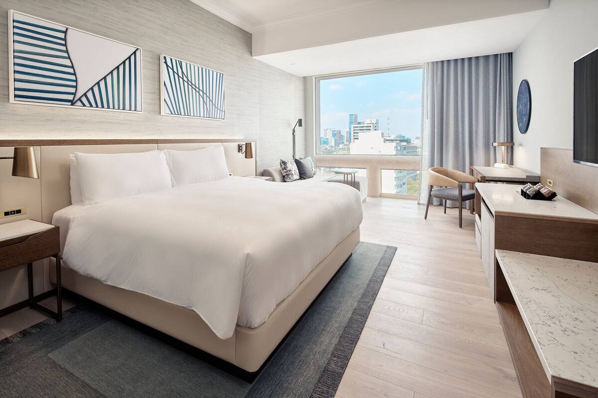 Een moderne hotelkamer met een groot bed, een bureau en uitzicht op de stad.