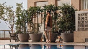 Un hombre caminando cerca de una piscina con macetas grandes y un edificio al fondo.