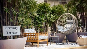 Una terraza Serenity con un banco de madera, una silla de mimbre y plantas en macetas.