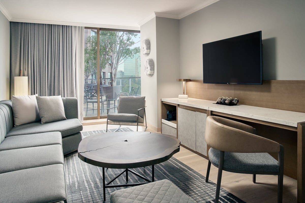 Een moderne hotelkamer met een bank, een ronde tafel, een televisie en een balkon met stoelen.